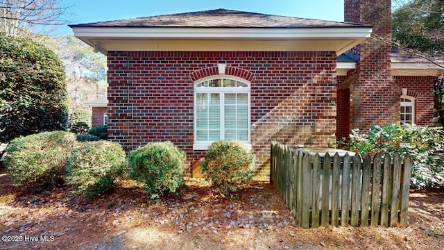 exterior space with brick siding, a chimney, and fence