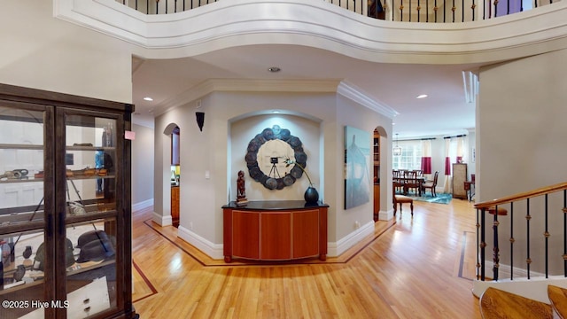 corridor with light wood-style flooring, arched walkways, and ornamental molding