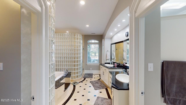 bathroom with baseboards, a tile shower, recessed lighting, a bath, and vanity