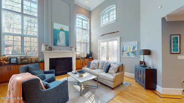 living area with light wood-style floors, a high ceiling, a fireplace, crown molding, and baseboards