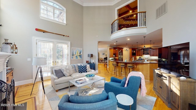 living room with a wealth of natural light, visible vents, crown molding, and light wood-style floors
