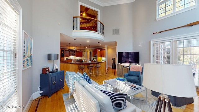 living room with visible vents, baseboards, light wood-style floors, and ornamental molding