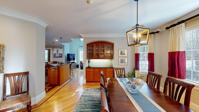 dining area featuring a wealth of natural light, light wood-type flooring, an inviting chandelier, and ornamental molding
