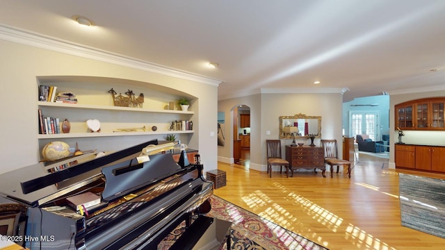 living area featuring built in features, light wood-style floors, arched walkways, and ornamental molding
