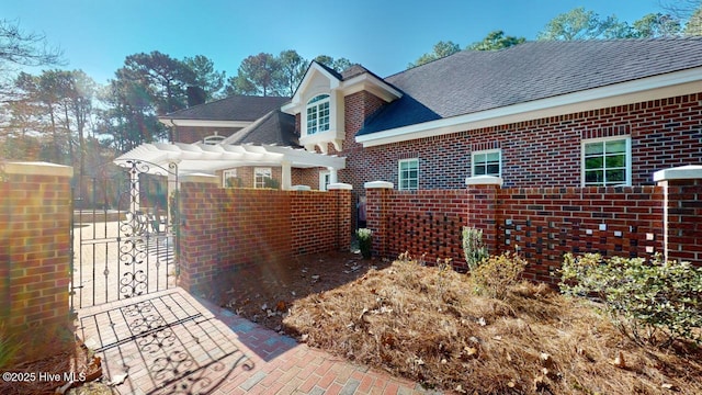 view of side of property with a pergola, a gate, fence, roof with shingles, and brick siding