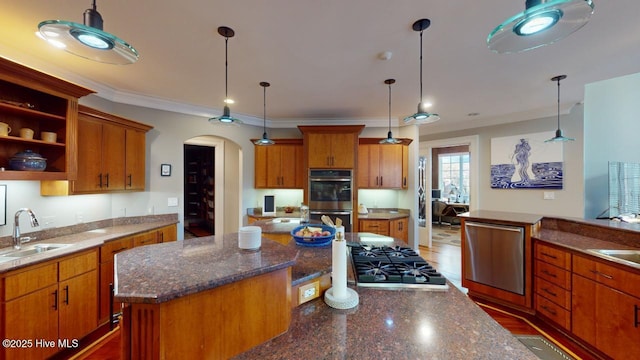kitchen featuring a kitchen island, brown cabinets, appliances with stainless steel finishes, arched walkways, and a sink
