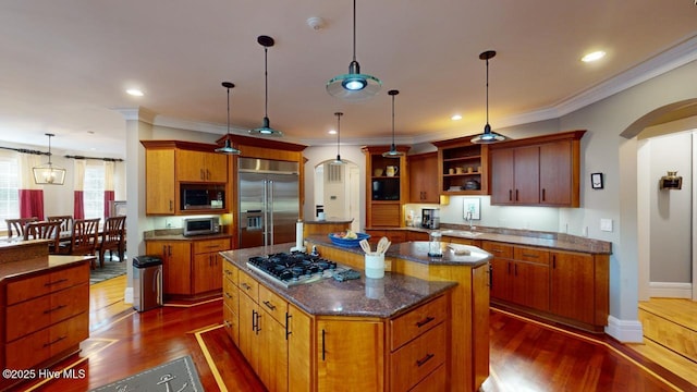 kitchen featuring arched walkways, built in appliances, a kitchen island, and dark wood-style flooring