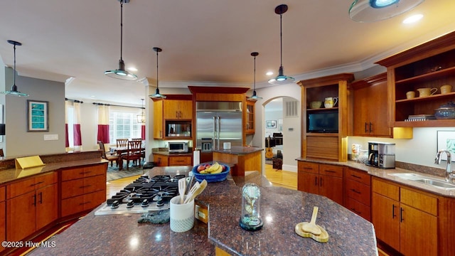 kitchen featuring a kitchen island, open shelves, ornamental molding, a sink, and built in appliances