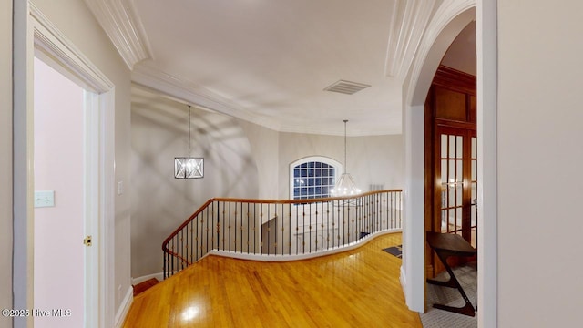 staircase featuring a notable chandelier, wood finished floors, visible vents, and ornamental molding
