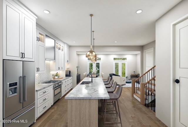 kitchen with white cabinets, premium appliances, a breakfast bar, a sink, and tasteful backsplash
