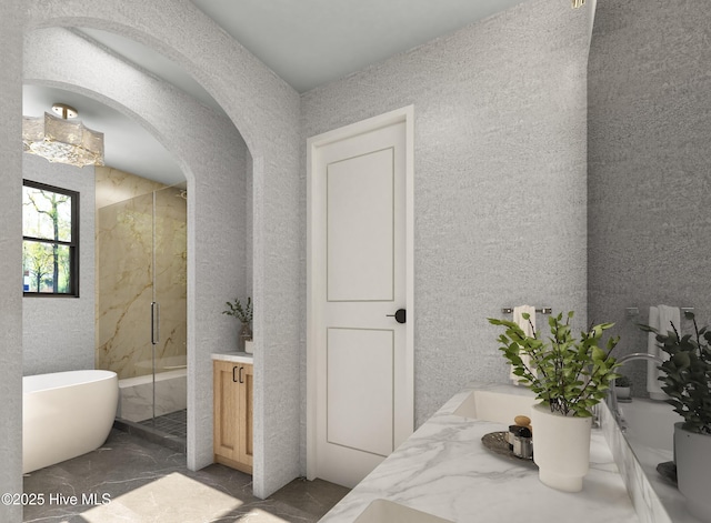 full bath with a marble finish shower, vanity, a freestanding tub, and a textured wall
