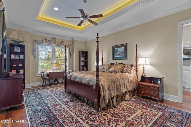 bedroom featuring a tray ceiling, wood finished floors, baseboards, and ornamental molding