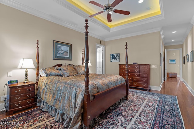 bedroom featuring a tray ceiling, wood finished floors, recessed lighting, crown molding, and baseboards