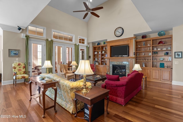 living area with a ceiling fan, wood finished floors, baseboards, high vaulted ceiling, and a glass covered fireplace