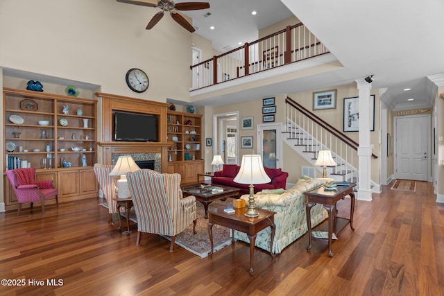 living area featuring stairway, ornamental molding, a fireplace, wood finished floors, and a ceiling fan