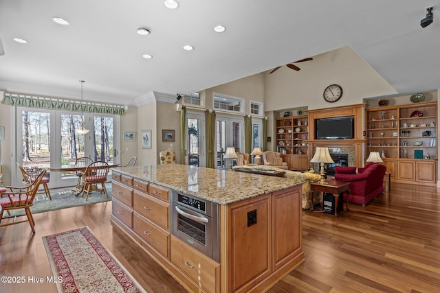 kitchen with wood finished floors, light stone countertops, a ceiling fan, a glass covered fireplace, and stainless steel oven