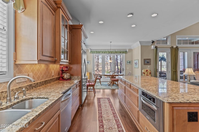 kitchen featuring brown cabinetry, dark wood-style flooring, a sink, appliances with stainless steel finishes, and backsplash