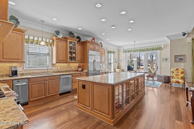kitchen featuring a sink, a kitchen island, wood finished floors, appliances with stainless steel finishes, and glass insert cabinets
