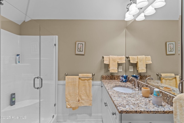 full bath featuring a wainscoted wall, a stall shower, vanity, and lofted ceiling