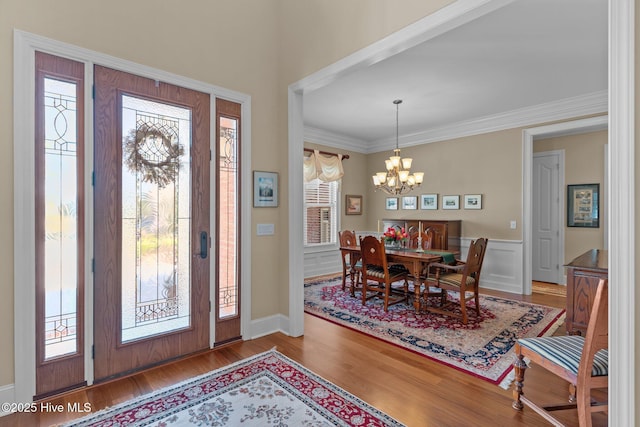 entryway featuring ornamental molding, wood finished floors, an inviting chandelier, wainscoting, and a decorative wall