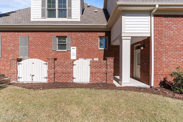 rear view of property featuring a gate, a lawn, and brick siding