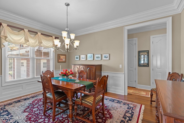 dining room featuring ornamental molding, wood finished floors, a wainscoted wall, and a chandelier