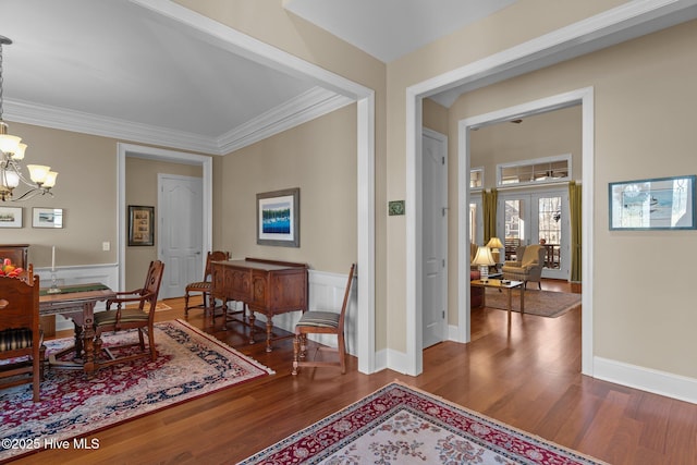 dining space with a wainscoted wall, wood finished floors, a chandelier, and ornamental molding