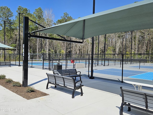 view of property's community featuring a forest view, a tennis court, and fence
