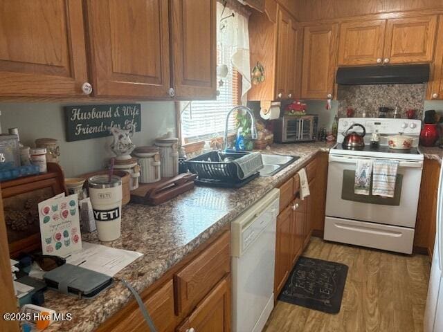 kitchen with brown cabinets, under cabinet range hood, a sink, white appliances, and light wood finished floors