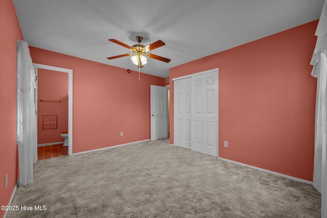 unfurnished bedroom with a ceiling fan, carpet floors, ensuite bath, a closet, and a textured ceiling