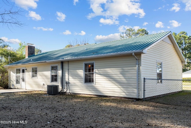 rear view of house with a chimney, cooling unit, metal roof, and fence