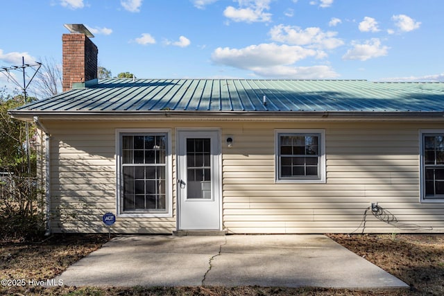 property entrance featuring metal roof, a patio, and a chimney