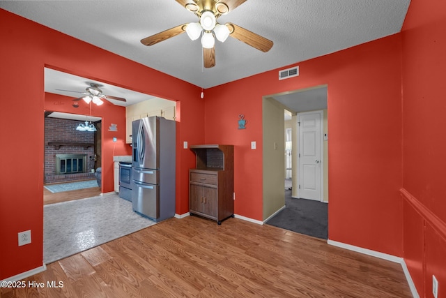 kitchen featuring visible vents, light wood finished floors, a fireplace, ceiling fan, and appliances with stainless steel finishes