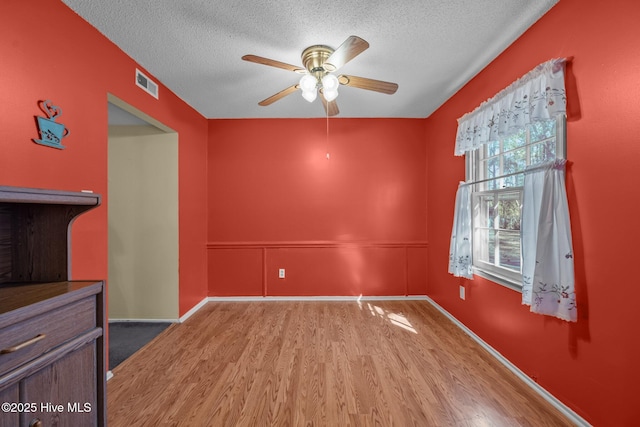 unfurnished room with wood finished floors, baseboards, a ceiling fan, visible vents, and a textured ceiling