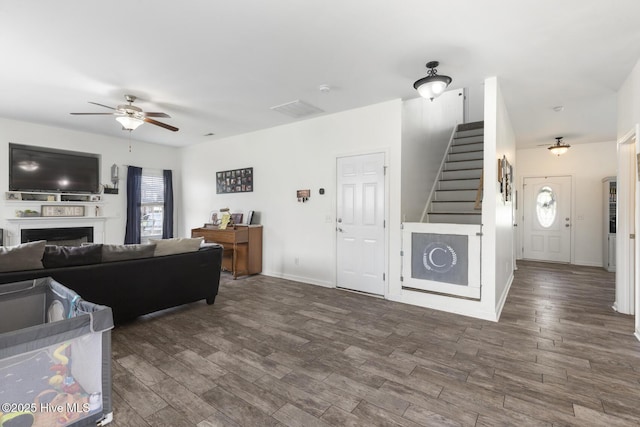 living area featuring wood finished floors, a ceiling fan, visible vents, a fireplace, and stairs