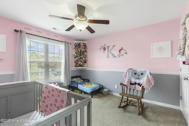 carpeted bedroom with visible vents, a crib, baseboards, and a ceiling fan