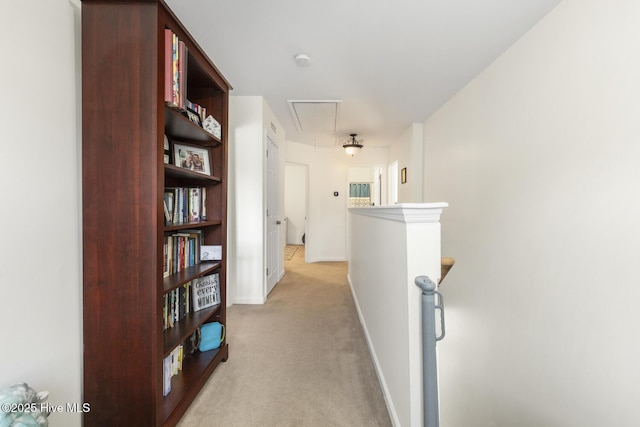hall featuring attic access, an upstairs landing, light colored carpet, and baseboards