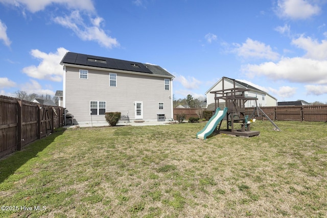 rear view of property with roof mounted solar panels, a lawn, a playground, and a fenced backyard