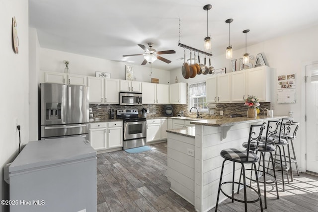 kitchen with a ceiling fan, wood finished floors, a peninsula, stainless steel appliances, and backsplash