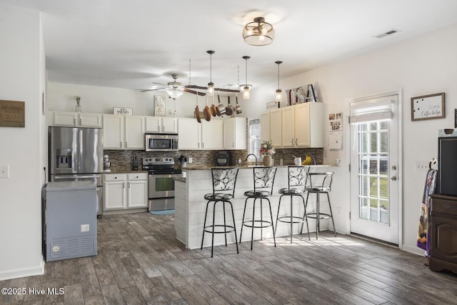 kitchen featuring a ceiling fan, backsplash, appliances with stainless steel finishes, a breakfast bar area, and dark wood-style flooring
