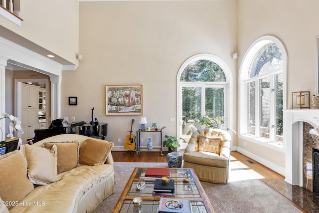 living area featuring wood finished floors, a towering ceiling, baseboards, and ornate columns