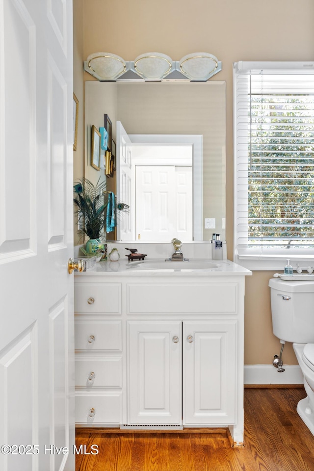 half bath featuring plenty of natural light, toilet, vanity, and wood finished floors