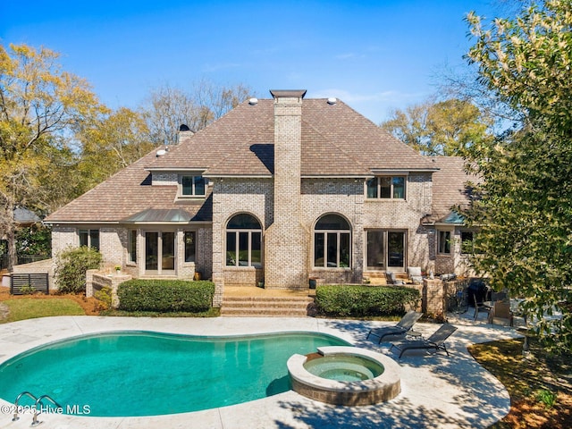 back of house with a patio area, a chimney, a shingled roof, brick siding, and a pool with connected hot tub