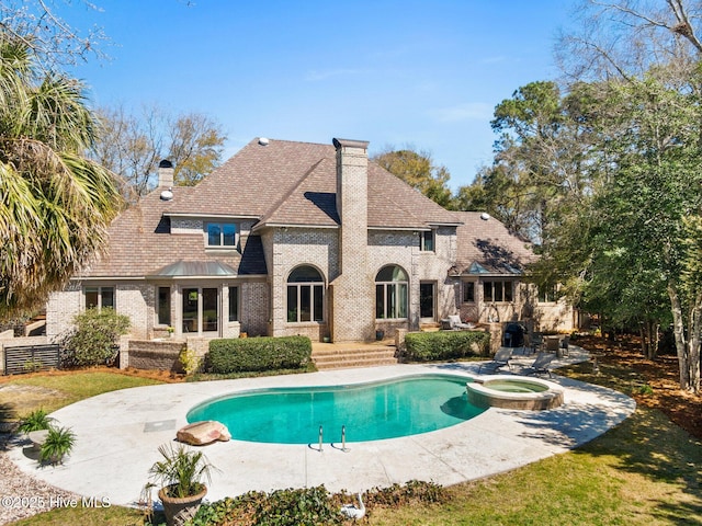 back of house with a chimney, brick siding, a patio area, a shingled roof, and a pool with connected hot tub