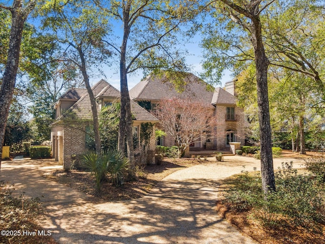view of front of property featuring a chimney, brick siding, and concrete driveway