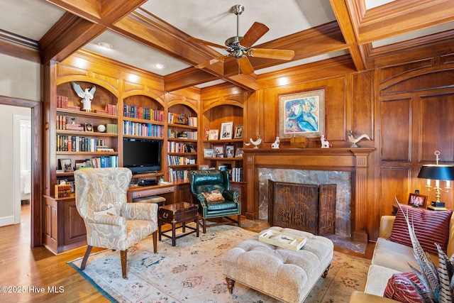 sitting room featuring a ceiling fan, crown molding, built in shelves, a fireplace, and coffered ceiling
