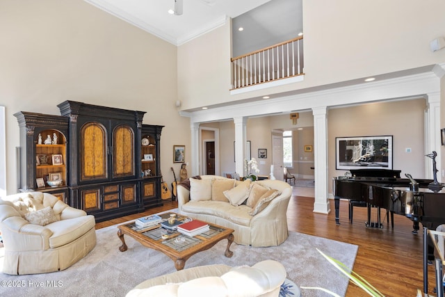 living area featuring wood finished floors, crown molding, a towering ceiling, and decorative columns