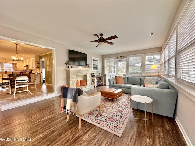 living room featuring baseboards, visible vents, ceiling fan with notable chandelier, wood finished floors, and a fireplace