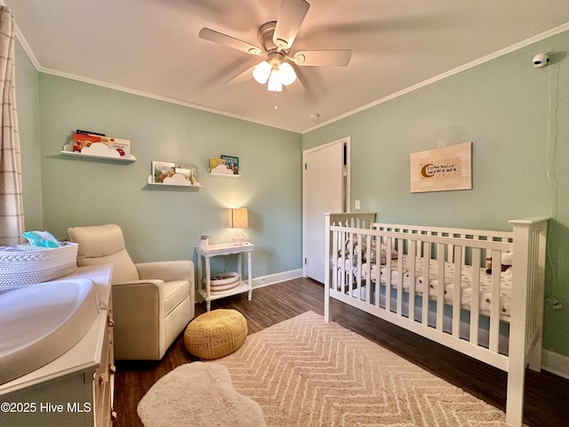 bedroom featuring baseboards, ornamental molding, wood finished floors, and a crib