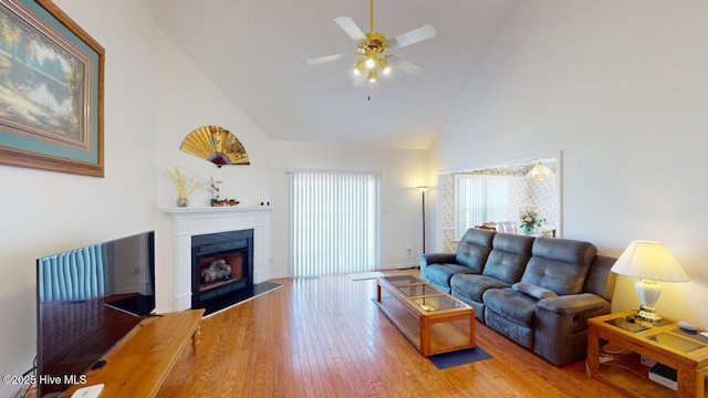 living area with baseboards, a fireplace with flush hearth, light wood-type flooring, high vaulted ceiling, and a ceiling fan